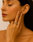 A woman with smooth, tan skin and straight dark hair touches her face, showcasing a Princess Goes Hollywood verstellbarer Ring aus Edelstahl. Her eyes are closed, and her neatly manicured nails are painted nude.