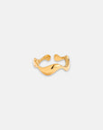 A Princess Goes Hollywood gold open ring with Gelbgold Vergoldung and a gently curving Edelstahl band rests on a plain light gray background, its shiny surface reflecting light and emphasizing its elegant, minimalist organic design.