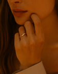 A close-up of a person’s hand wearing a Princess Goes Hollywood offener Ring mit Gelbgold Vergoldung, gently touching their face. Soft light adds warmth and highlights the golden tones, with only the lower half of their face visible.