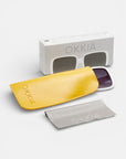 Okkia White Oversize quadratische Sonnenbrille mit dunklen Gläsern (UV 400 Schutz), präsentiert neben einem gelben Okkia-Etui, grauem Reinigungstuch und illustrierter weißer Okkia-Box auf weißem Hintergrund.