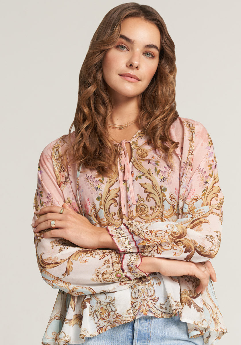 Eine Dame trägt eine Seidenbluse mit Ornamentprint und Rüschen