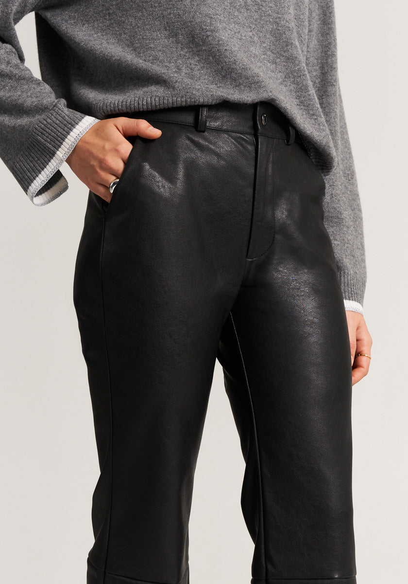 A person wears high-waisted black faux leather pants and a loose gray Feinstrickpullover with white-trimmed sleeves from Princess Goes Hollywood. One hand is in their pocket, the other by their side. The photo is cropped from mid-torso to below the knees.