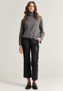 A woman with loose wavy hair stands against a plain background wearing a gray turtleneck sweater, black faux leather loafers, and flared zip-up trousers from Princess Goes Hollywood. She gazes confidently at the camera, her left hand in her pocket.