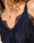 A close-up of a woman in a navy blue satin camisole with lace trim by Princess Goes Hollywood, wearing a stainless steel 304 retro-style necklace with a rectangular pendant. Only her neck and upper chest are visible; she has light brown wavy hair.