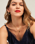 A woman with wavy light brown hair wears a navy lace-trimmed camisole and a Retro-Stil Halskette mit rechteckigem Anhänger from Princess Goes Hollywood, plus gold hoop earrings, gazing confidently at the camera with red lipstick against a neutral background.