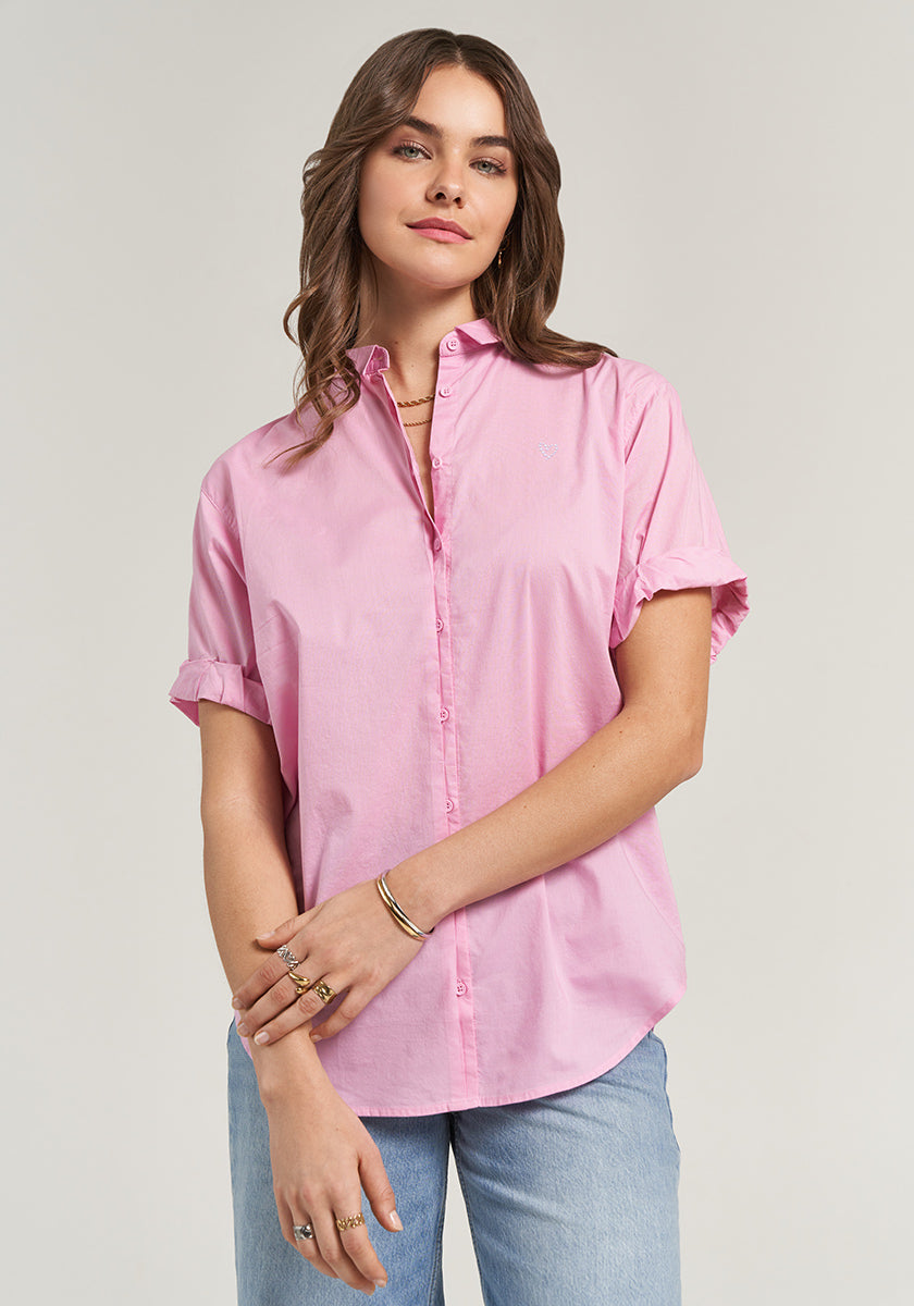 A woman with light wavy hair wears a light pink Princess Goes Hollywood Hemd with rolled sleeves and light blue jeans, standing facing forward with a relaxed expression, minimal jewelry, and arms loosely crossed against a plain background.