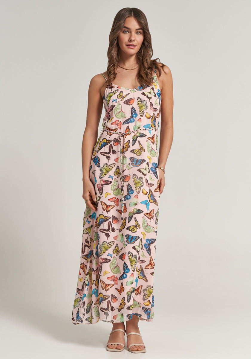 A woman with loose brown hair faces forward in a sleeveless, floor-length Princess Goes Hollywood Midikleid featuring colorful butterfly prints on pale pink. Beige sandals and a bracelet finish her look against a plain light background.