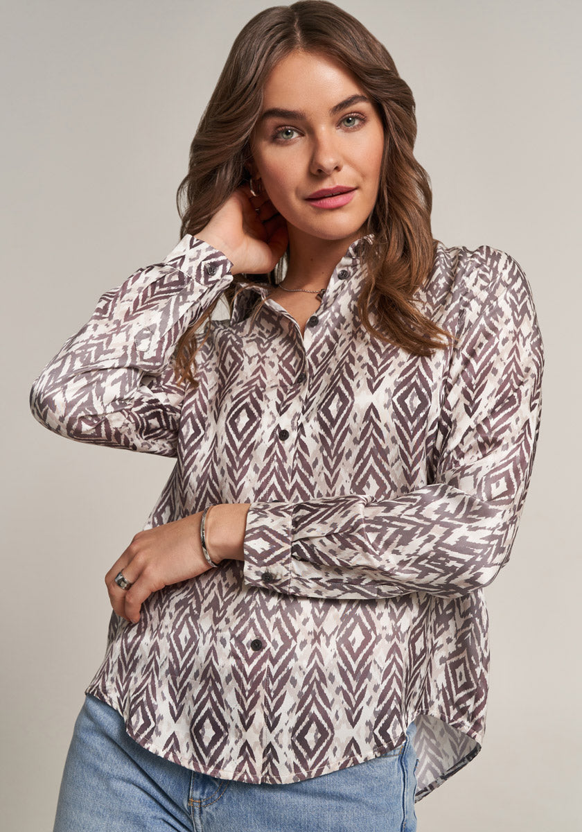 A woman with long brown hair models a Princess Goes Hollywood Hemdbluse with a brown and white geometric print and elegant silk content, standing against a neutral background and looking confidently at the camera.