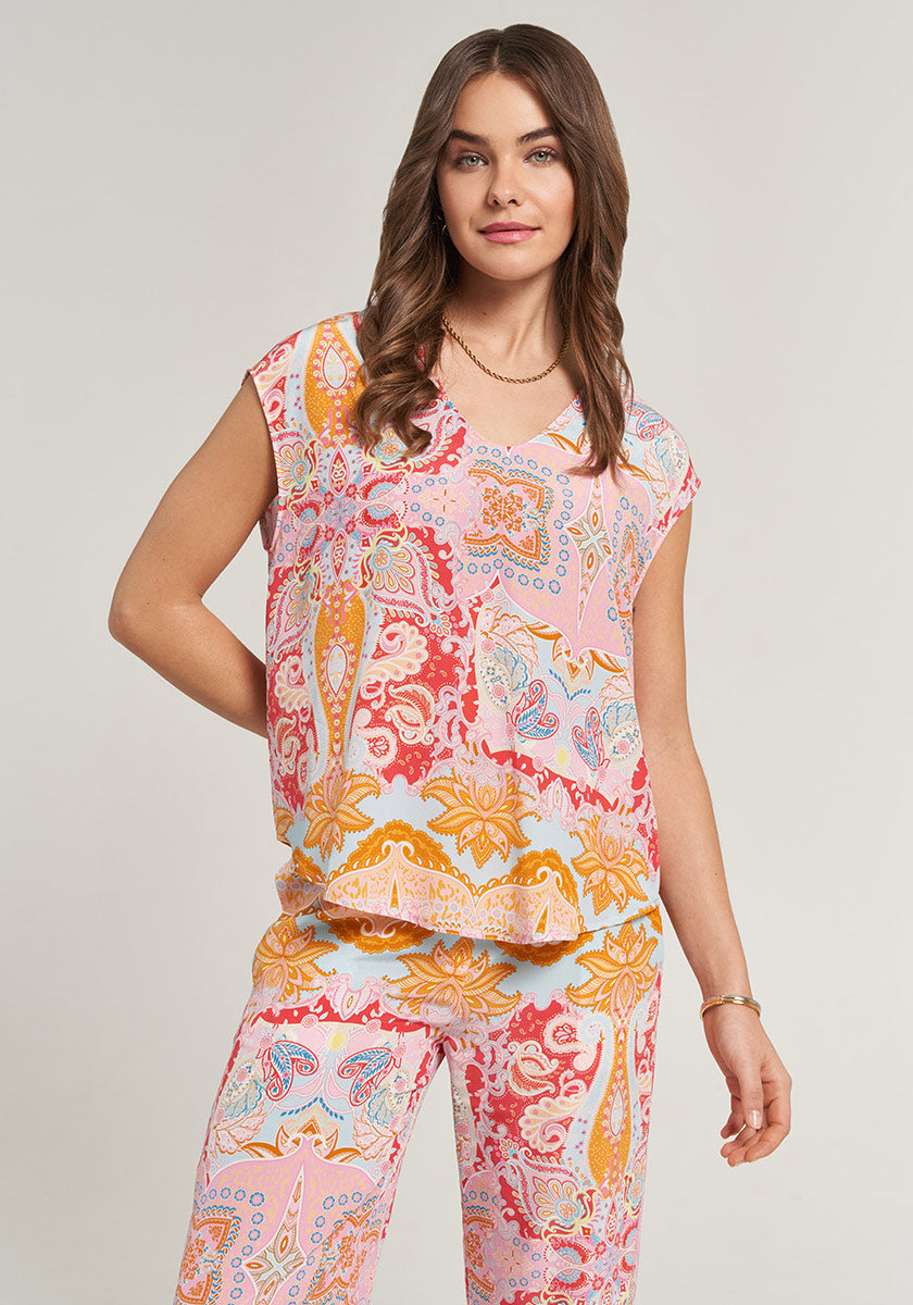 A woman with long brown hair wears a colorful, short-sleeved top and matching pants by Princess Goes Hollywood, featuring an ornate print in 100% silk for comfortable wear as she smiles against a light background.