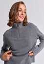 A woman with shoulder-length brown hair smiles, looking to the side. She wears a gray Princess Goes Hollywood wool-cashmere blend half-zip mock neck sweater, tugging at the hem, against a plain light gray background.