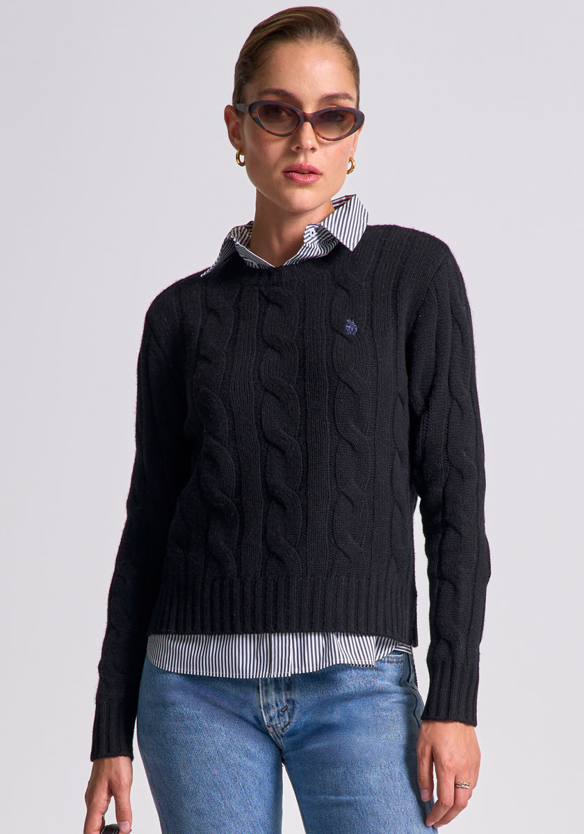 A woman stands facing forward against a plain light background wearing brown cat-eye sunglasses, gold hoop earrings, blue jeans, and a black cable-knit Regular Fit Wolle-Kaschmir-Mix Pullover by Princess Goes Hollywood over a striped shirt.