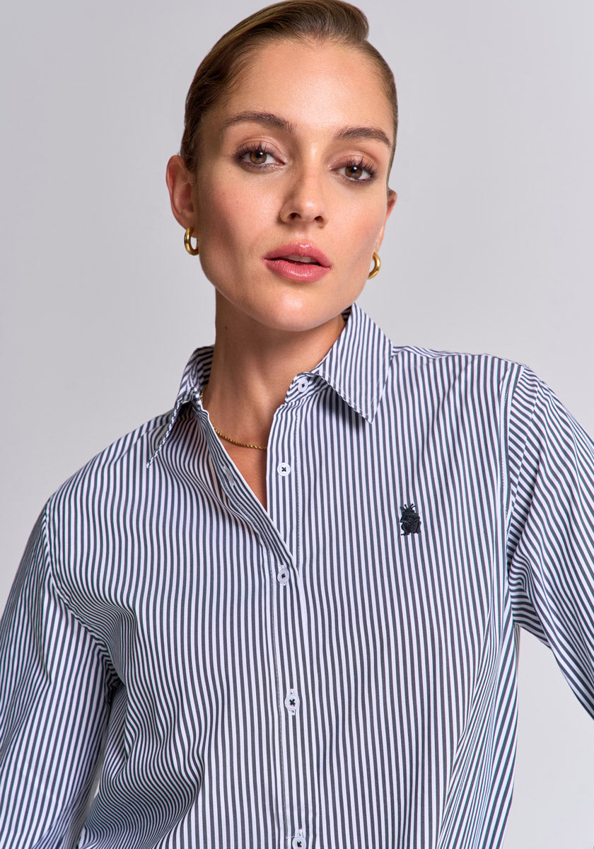 A woman with slicked-back hair, gold hoop earrings, and a subtle necklace models a Princess Goes Hollywood gestreiftes Baumwollhemd im Regular Fit mit Polokragen und kleinem gesticktem Logo, looking confidently at the camera against a plain gray background.