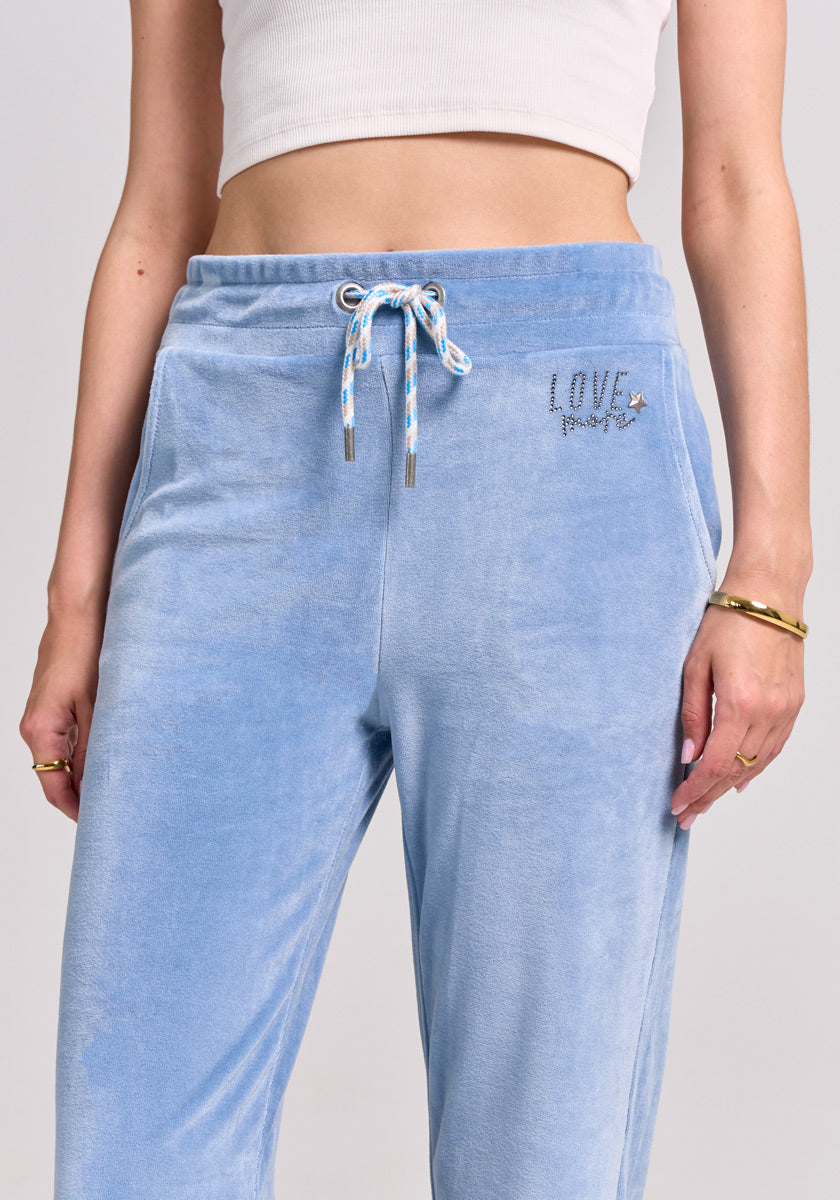 A person wears light blue Princess Goes Hollywood Nicki-Stoff sweatpants with a drawstring waist and LOVE embroidered near the pocket, paired with a white ribbed crop top and gold bangles, set against a neutral background.