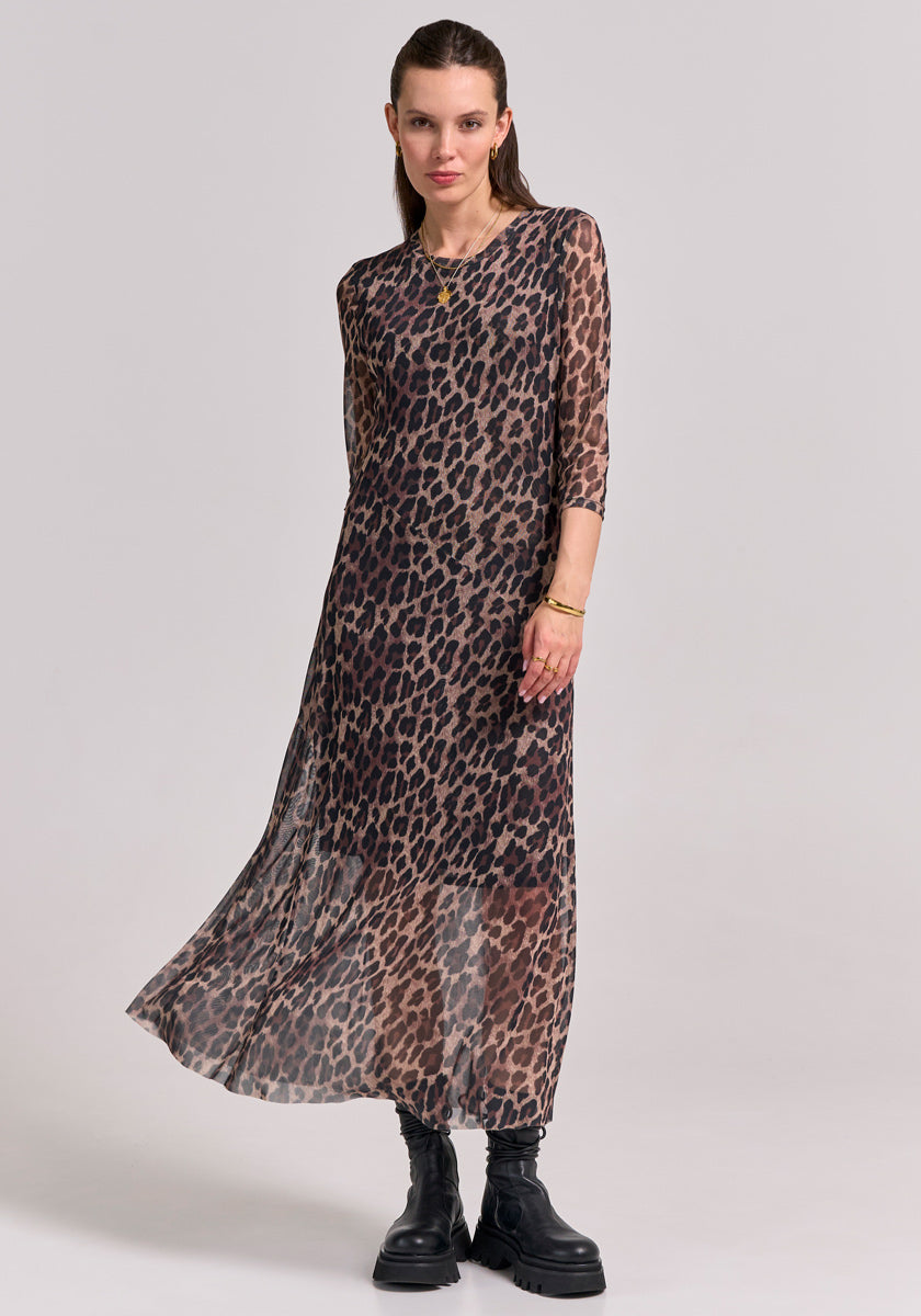 A woman poses against a light gray background in a sheer, ankle-length Glam-Leo-Print Mesh Kleid by Princess Goes Hollywood with three-quarter sleeves, chunky black boots, gold jewelry, and slicked-back brown hair.