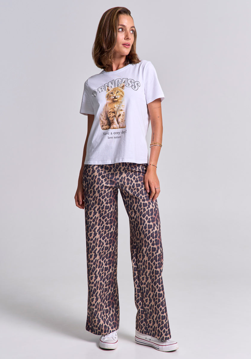 A woman with light brown hair and bracelets wears a Princess Goes Hollywood white Baumwolle T-shirt featuring a cat and “PRINCESS” motif, paired with loose Luchs-Print pants and white sneakers, standing against a plain background, smiling slightly.