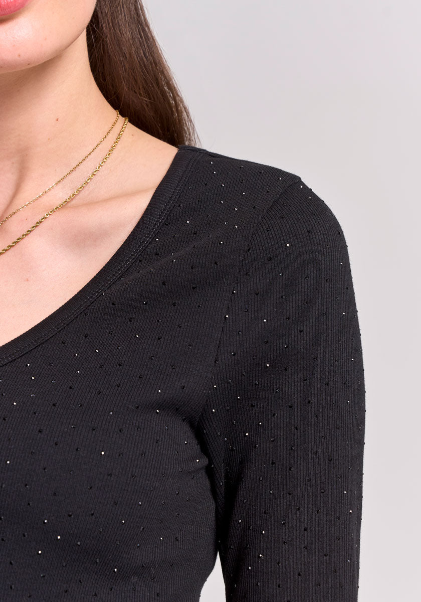 Close-up of a woman in a black, long-sleeved cotton shirt with subtle rhinestone accents by Princess Goes Hollywood. She has long brown hair and wears two thin gold necklaces; only her lower face, neck, and upper torso are visible.