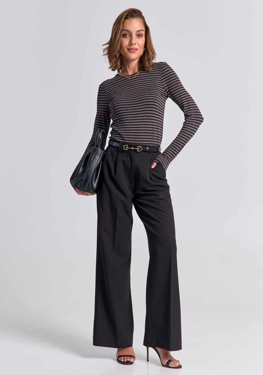 A woman with shoulder-length hair and a relaxed smile stands confidently against a plain backdrop, wearing a Princess Goes Hollywood gestreiftes Langarmshirt with Stretchanteil, tucked into high-waisted black wide-leg trousers.