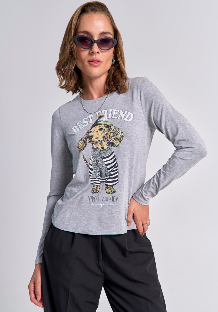 A woman with wavy light brown hair confidently poses in cat-eye sunglasses, black trousers, and a gray Princess Goes Hollywood Langarmshirt with Dackel-Print and “BEST FRIEND LOVE-PEACE-JOY” text against a plain light background.