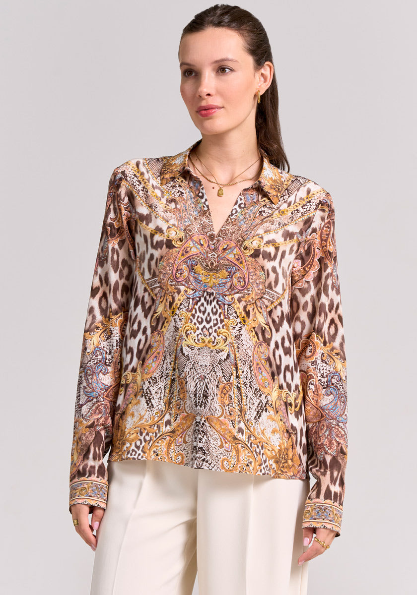 A woman with fair skin and brown hair tied back models a Princess Goes Hollywood Seidenbluse with Snake-Leo-Print and paisley in brown, beige, and gold, paired with cream pants and gold jewelry against a light background.