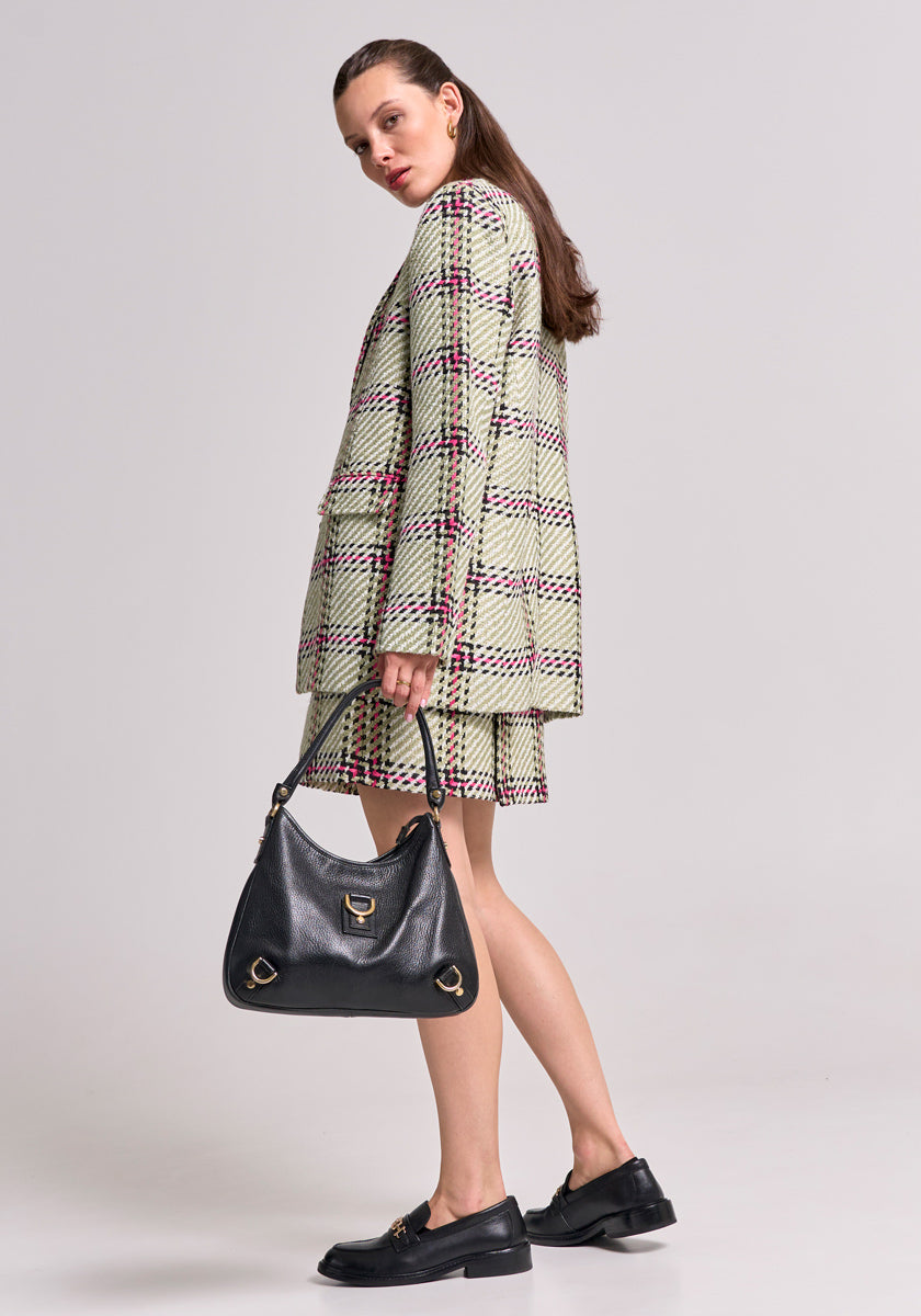 A woman stands in profile against a plain backdrop, wearing a light Karo-Print Blazer with Gürtelschlaufen and matching Tweed Minirock by Princess Goes Hollywood. She holds a black leather handbag with gold hardware, hair tucked behind one ear.