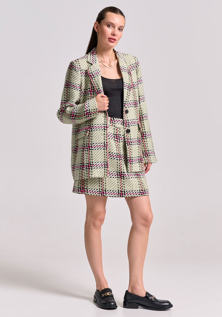 A woman faces forward in a Princess Goes Hollywood Karo-Print Tweed Minirock and matching blazer with red and black lines, paired with a black top and loafers. Her straight hair is tucked behind her ears. The background is plain light gray.