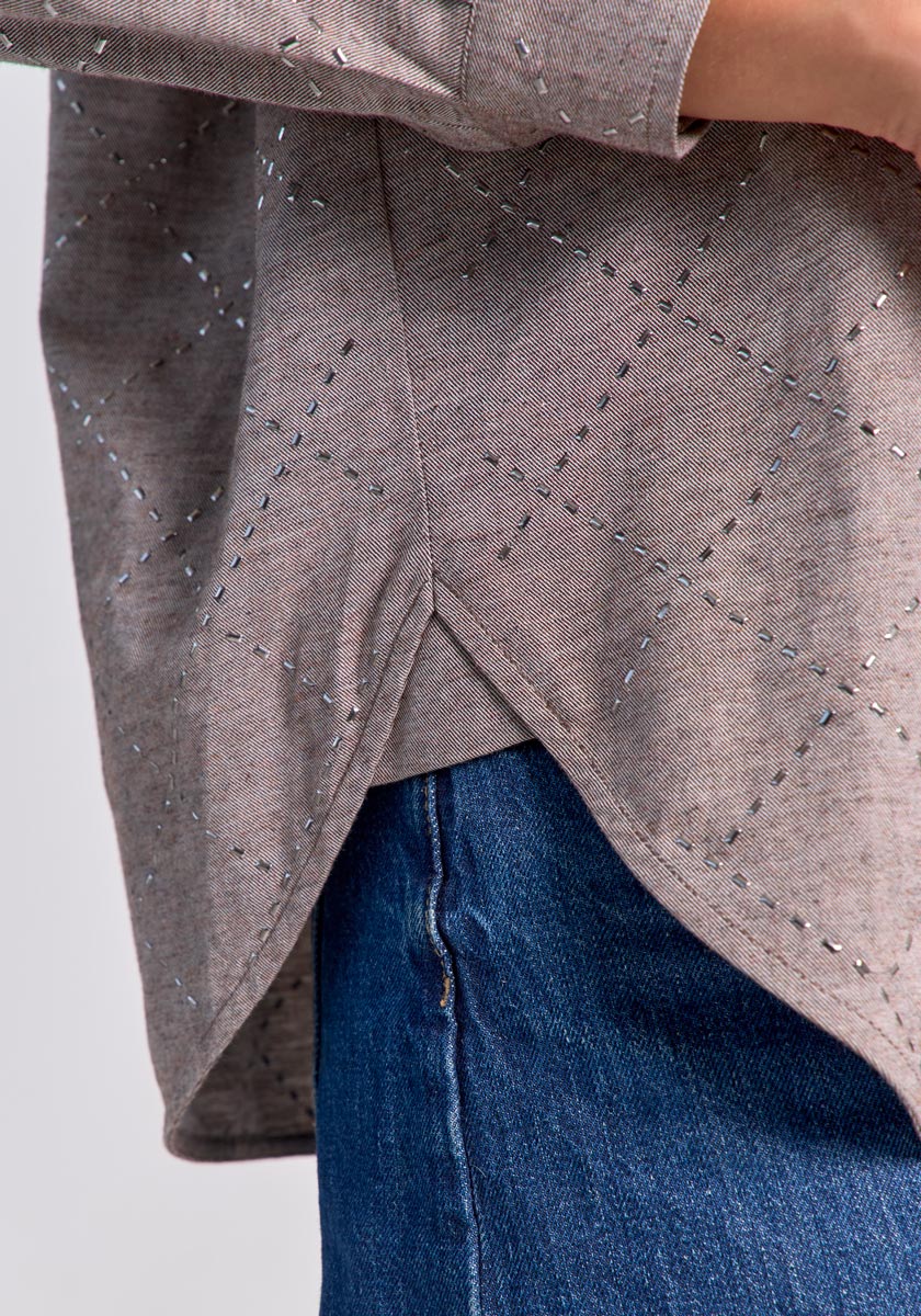 Close-up of a person wearing a light brown, long-sleeve cotton blouse by Princess Goes Hollywood with a diamond stitch pattern and overlapping hem, paired with blue jeans. Only the torso and upper hip are visible; background is plain and light.
