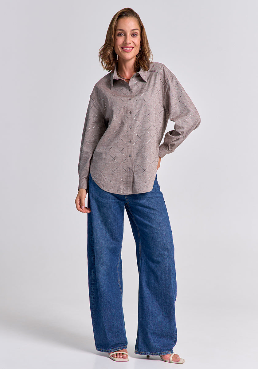 A woman smiles in a relaxed pose against a plain background, wearing a Princess Goes Hollywood cotton patterned shirt, wide-leg blue jeans, and open-toe sandals. One hand is on her hip while the other hangs by her side.