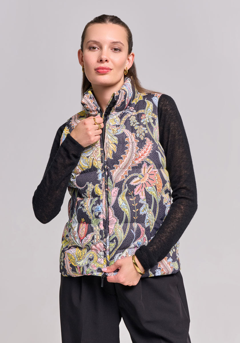 A woman with straight brown hair pulled back models a high-collared Paisley-Print Steppweste from Princess Goes Hollywood over a black top and pants, confidently touching her collar against a plain gray background.