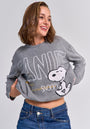 A woman with shoulder-length brown hair smiles to the side, wearing blue jeans and a gray Princess Goes Hollywood Peanuts Pullover. The Wolle-Kaschmir-Mix sweater features a Snoopy motif and bold “PEANUTS” and “SNOOPY” lettering.