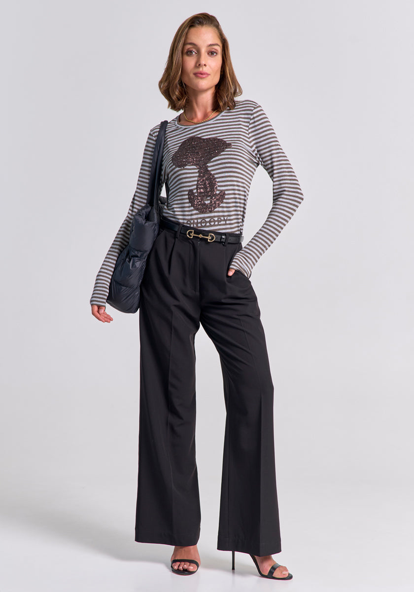 A woman with shoulder-length light brown hair poses against a plain background wearing a Princess Goes Hollywood gestreiftes Langarmshirt mit Paillettenbesatz, high-waisted black wide-leg trousers, black heeled sandals, a black belt, and a dark shoulder bag.