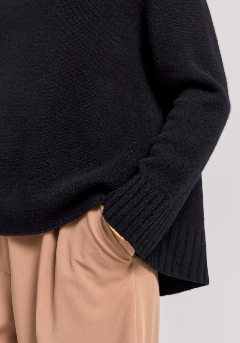 A person wears a loose Frogbox by Princess Merinowolle Pullover with ribbed cuffs and has their right hand in the pocket of light tan pleated pants. The image is cropped to show only the torso and upper legs against a neutral background.