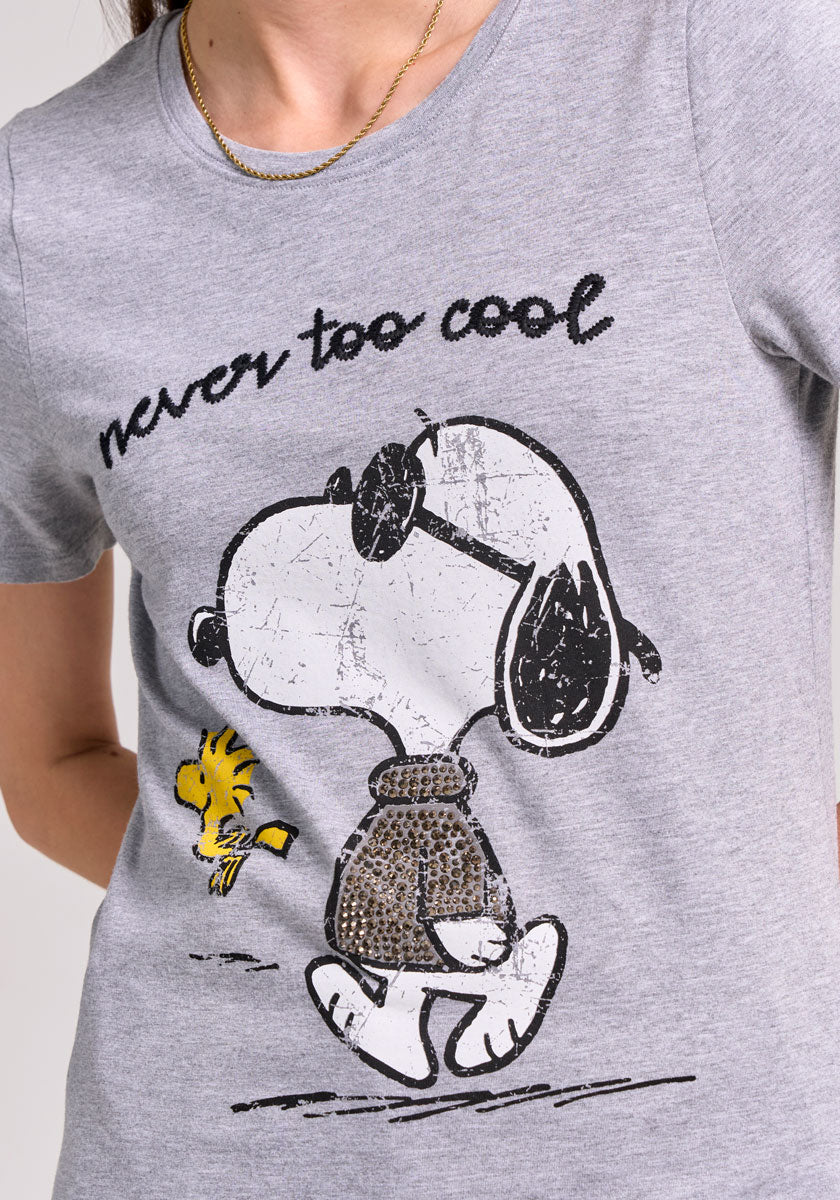 A person wears a Frogbox by Princess Snoopy T-shirt with a round neckline, showing Snoopy in a brown sweater walking with Woodstock. Above them, handwritten text reads never too cool. The person’s head is partly out of frame.