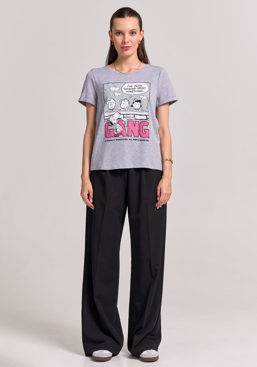 A woman faces forward against a plain background, wearing a Frogbox by Princess gray Peanuts-Print T-Shirt mit Stretch, loose black trousers, and gray sneakers. Her brown hair is pulled back, arms relaxed at her sides, expression neutral.