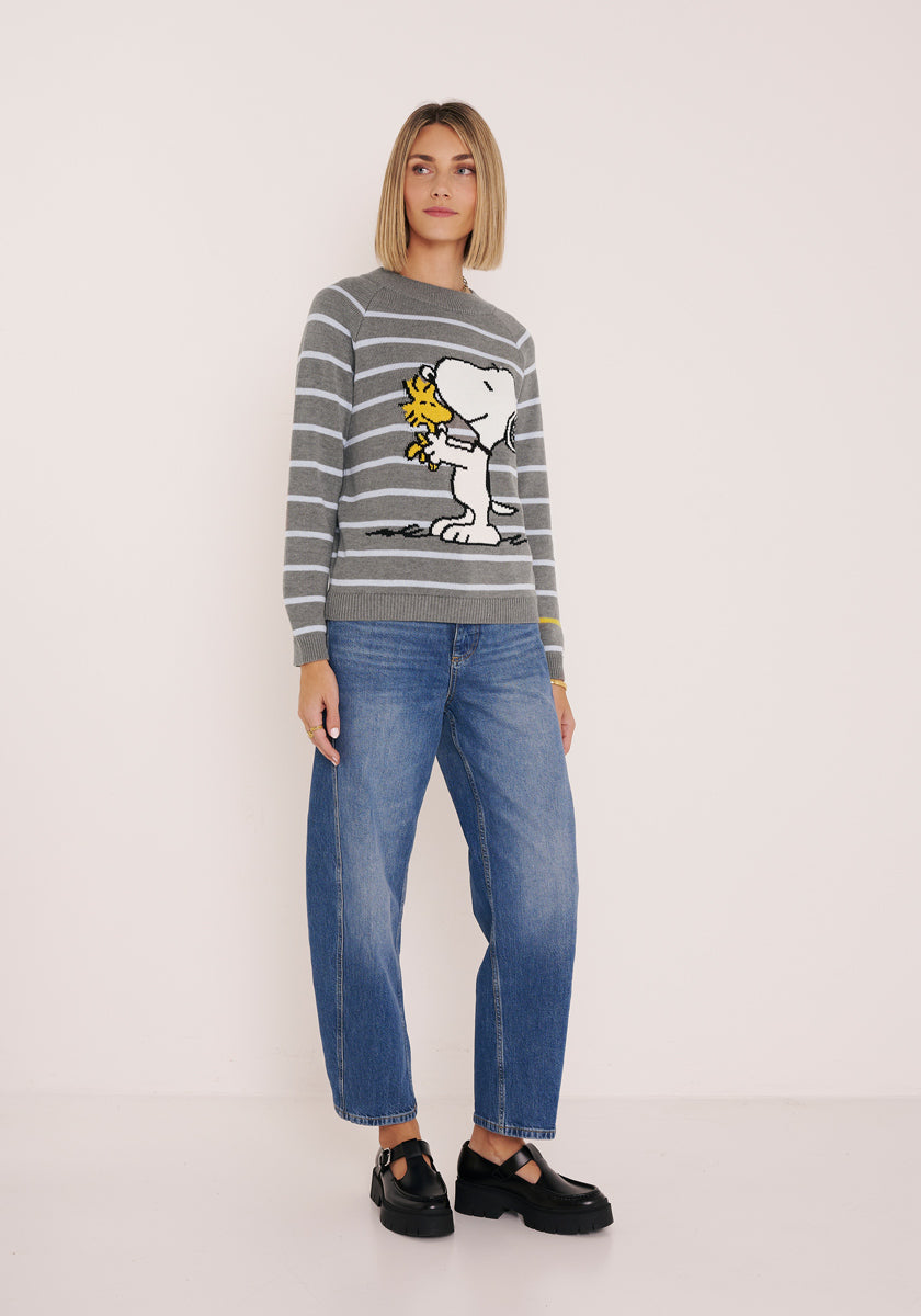 Eine Frau mit glattem blondem Haar trägt einen gestreiften Pullover aus Baumwollmix mit Snoopy und Woodstock von Princess Goes Hollywood, lockeren blauen Jeans und schwarzen Schuhen. Sie steht vor weißem Hintergrund und blickt neutral nach vorne.