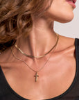 A woman with wavy brown hair wears a black top and two gold Princess Goes Hollywood necklaces—a Schlangenkette choker and a longer chain with a small Kreuzanhänger—against a neutral background, showing only her lower face and neck.
