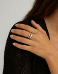 A woman with long brown hair wears a black textured garment by Princess Goes Hollywood. Her hand with neatly manicured nails rests on her chest, displaying a two-tone adjustable stainless steel ring—gold and silver—on her middle finger.