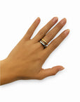 A left hand with light brown skin and manicured nails is shown against a white background, wearing on the ring finger a Princess Goes Hollywood zweifarbig Edelstahl Ring, a gold band, and a silver ring with white stones.
