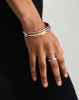 A close-up of a hand wearing a zweifarbig Edelstahl Ring by Princess Goes Hollywood and three stacked metallic bangles in gold, silver, and rose gold tones against ribbed black fabric for a minimalist, elegant look.