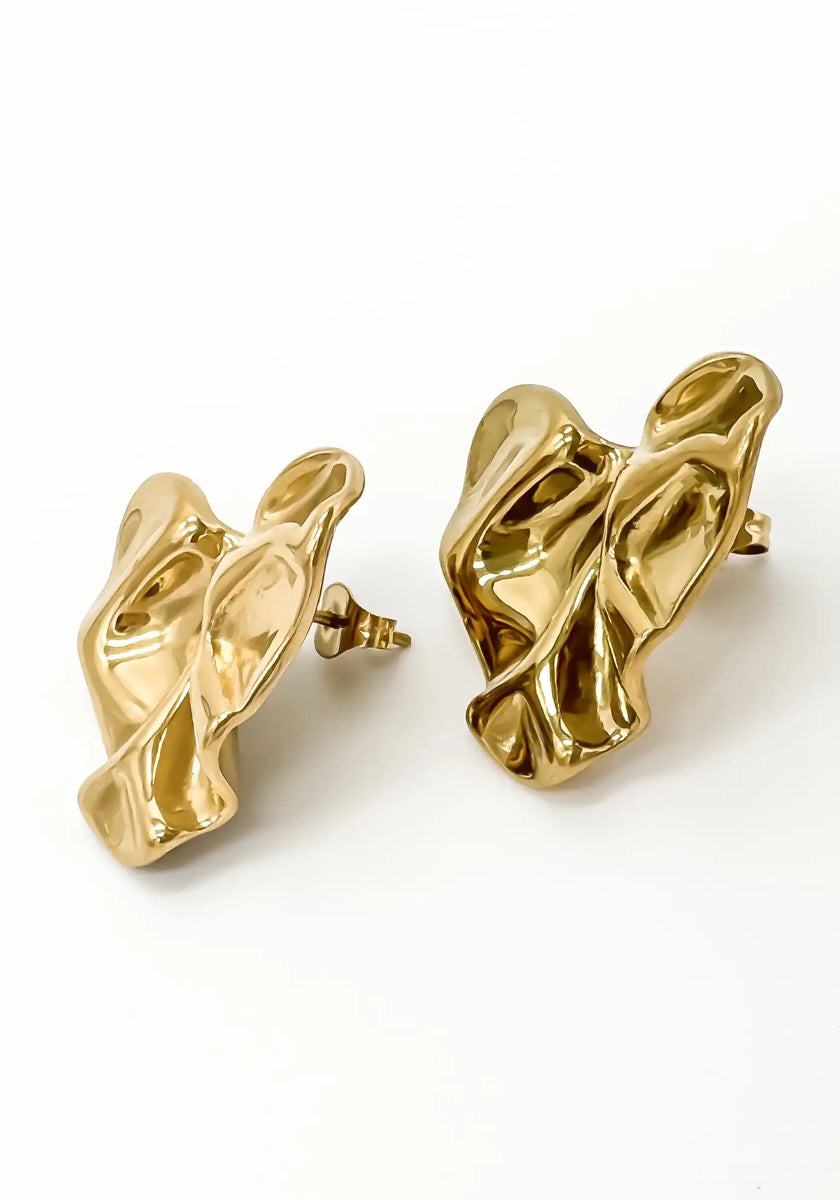 A pair of abstract, sculptural gold earrings by Princess Goes Hollywood with a glänzende Oberfläche, twisted organische Form, Edelstahl Ohrstecker, and reflective surfaces for a modern, artistic look against a plain white background.