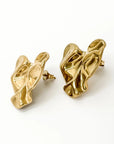 A pair of abstract, sculptural gold earrings by Princess Goes Hollywood with a glänzende Oberfläche, twisted organische Form, Edelstahl Ohrstecker, and reflective surfaces for a modern, artistic look against a plain white background.