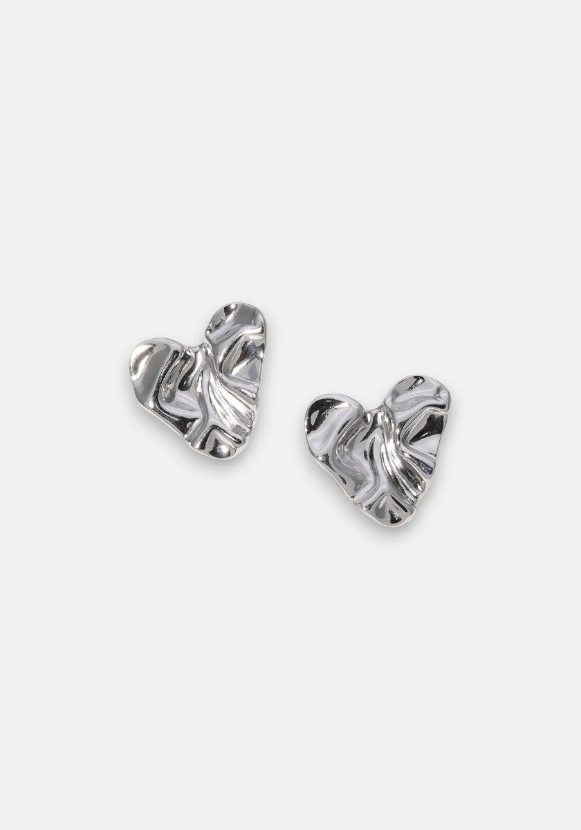 A pair of small, metallic heart-shaped Ohrstecker by Princess Goes Hollywood, crafted from Edelstahl with a textured, wavy surface that creates an abstract organic form and beautifully reflects light against a plain gray background.