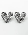 A pair of shiny, silver-toned Edelstahl Ohrstecker by Princess Goes Hollywood, shaped like abstract crumpled hearts. Their organische Form and wavy texture create a glänzende Oberfläche that beautifully reflects light.