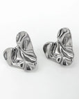 A pair of abstract, silver-toned Edelstahl Ohrstecker by Princess Goes Hollywood, shaped like irregular, crumpled hearts with a glänzende Oberfläche and textured folds. Shown on a plain white background.