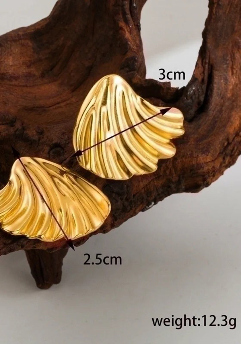A pair of gold, shell-shaped Ohrstecker by Princess Goes Hollywood rests on textured brown wood. Made from Edelstahl with 18K Goldbeschichtung, one earring measures 3 cm wide, 2.5 cm tall; weight: 12.3g shown in the corner.