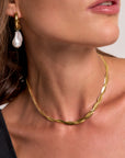 A close-up of a womans lower face and neck shows her wearing a Princess Goes Hollywood 18K gold-plated chain necklace and chunky gold hoop earring with a dangling irregular white pearl. Her glossy lips, black top, and brown hair complete the look.