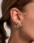 Close-up of a womans ear wearing Princess Goes Hollywoods bold, abstract earring in shiny 18K gold and silver Edelstahl with a wavy bicolor design, contrasting against her smooth skin and pulled-back brown hair.