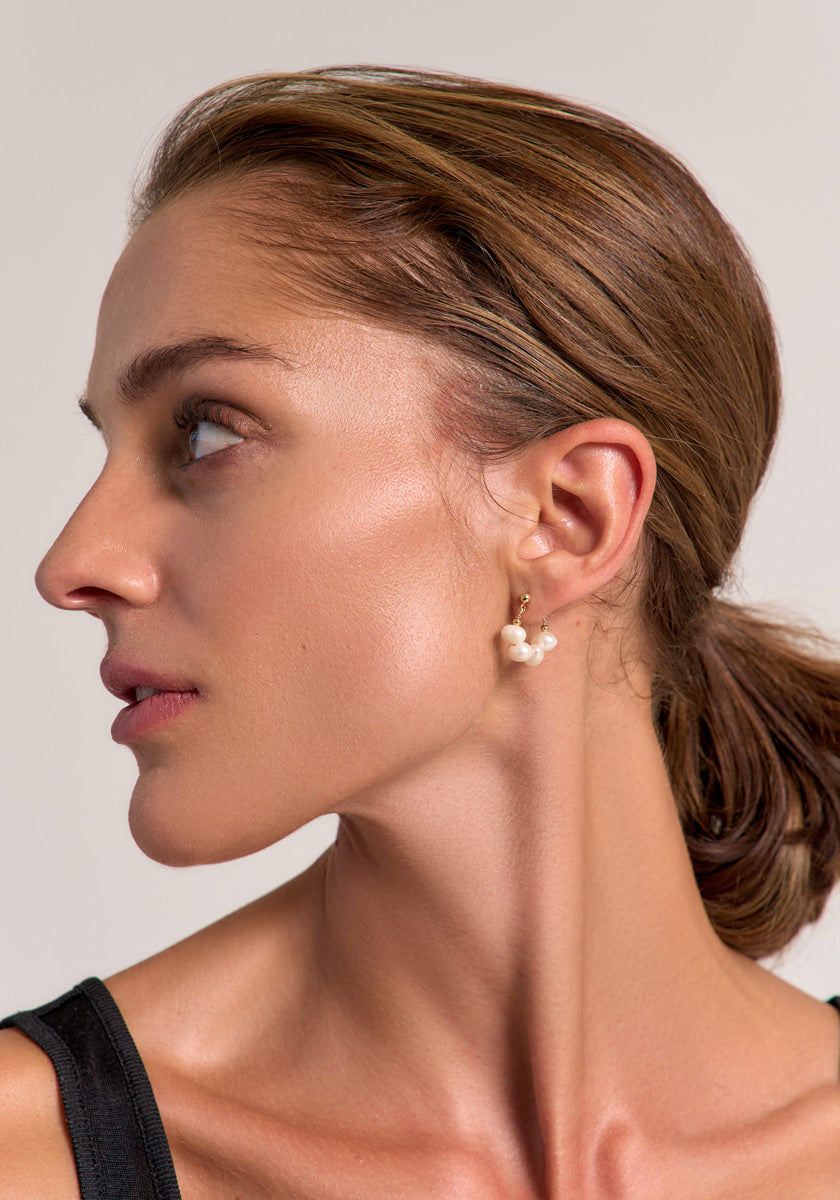 A woman with light skin and brown hair pulled back wears elegant Princess Goes Hollywood black creolen earrings with freshwater pearls on 925 sterling silver. She looks to the left, her natural glow standing out against a plain background.