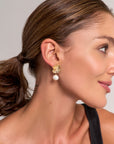 A woman with smooth, tan skin and brown hair in a low ponytail wears Princess Goes Hollywood gold floral 925 sterling silver stud earrings with a freshwater pearl. She is shown from the side, wearing a black tank top and softly smiling against a neutral background.