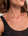 A woman with short brown hair wears a black sleeveless top and a Princess Goes Hollywood Edelstahl Halskette mit Süsswasserperlen: delicate gold necklace with evenly spaced pearls, a central large pearl pendant, and matching pearl earring.