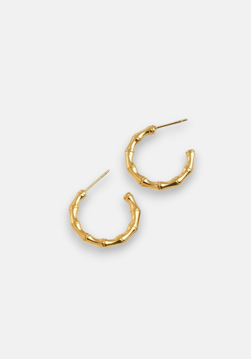 A pair of vergoldete Creolen in Bambus-Optik by Princess Goes Hollywood, featuring subtle bends and raised segments. Displayed on a white background, the elegant gold hoops have posts pointing in opposite directions.